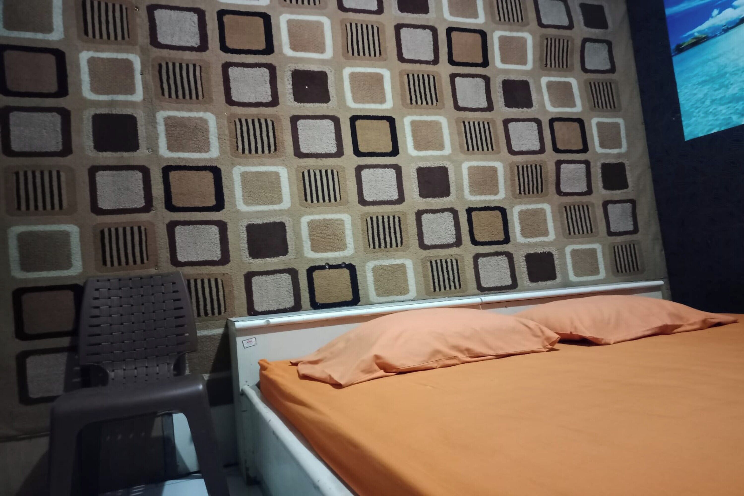 A room with a patterned wall, a bed with an orange bedspread, and a small stool.