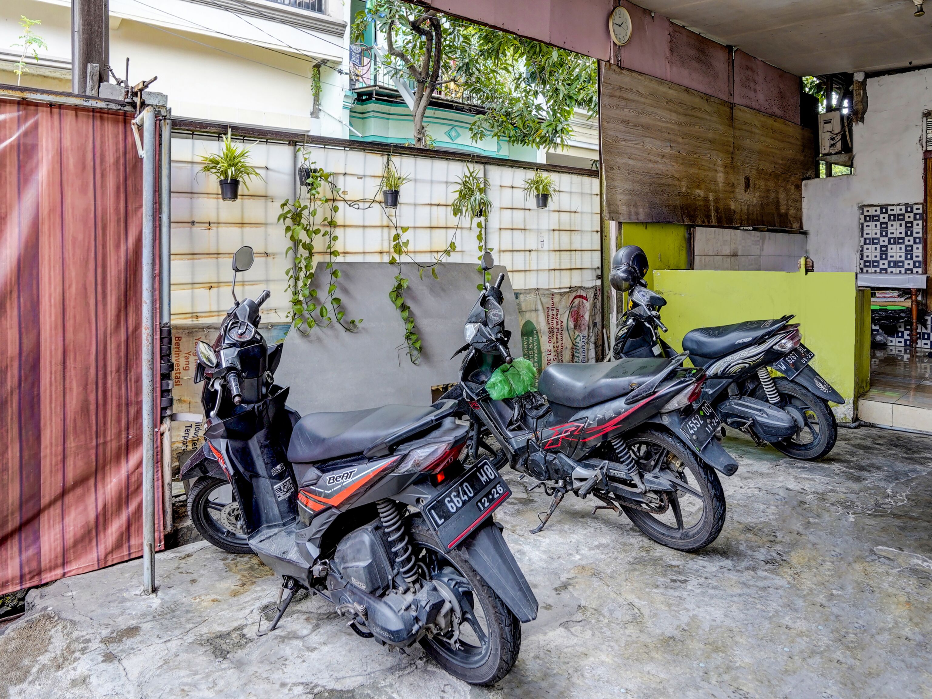 Two motorcycles parked in a covered area with a concrete floor, a wooden wall, and a green door.