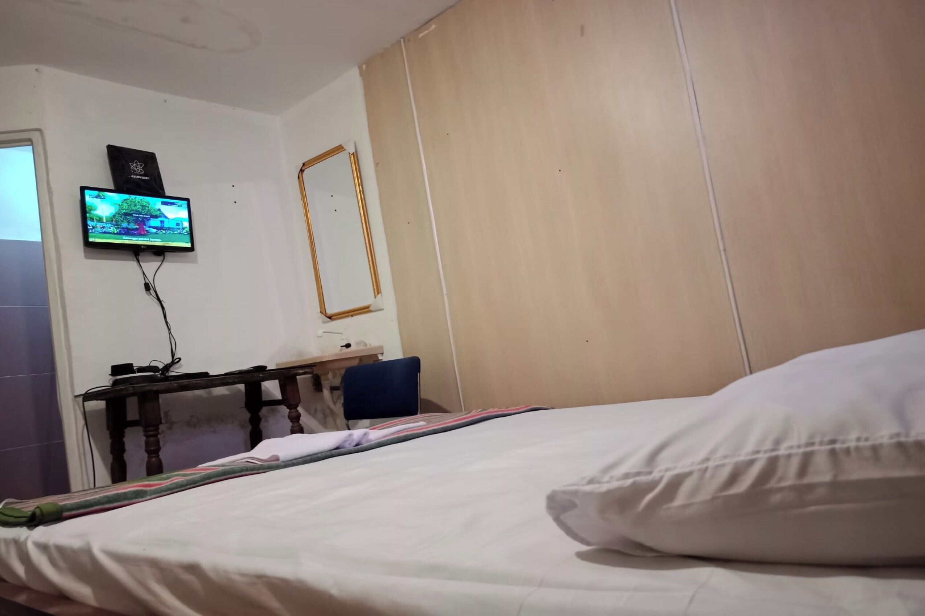Une chambre d’hôtel avec un lit, un bureau équipé d’un ordinateur, un téléviseur fixé au mur et une tête de lit en bois.