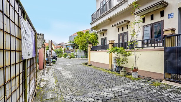 Una estrecha calle adoquinada flanqueada por edificios residenciales, con balcones y plantas en macetas.