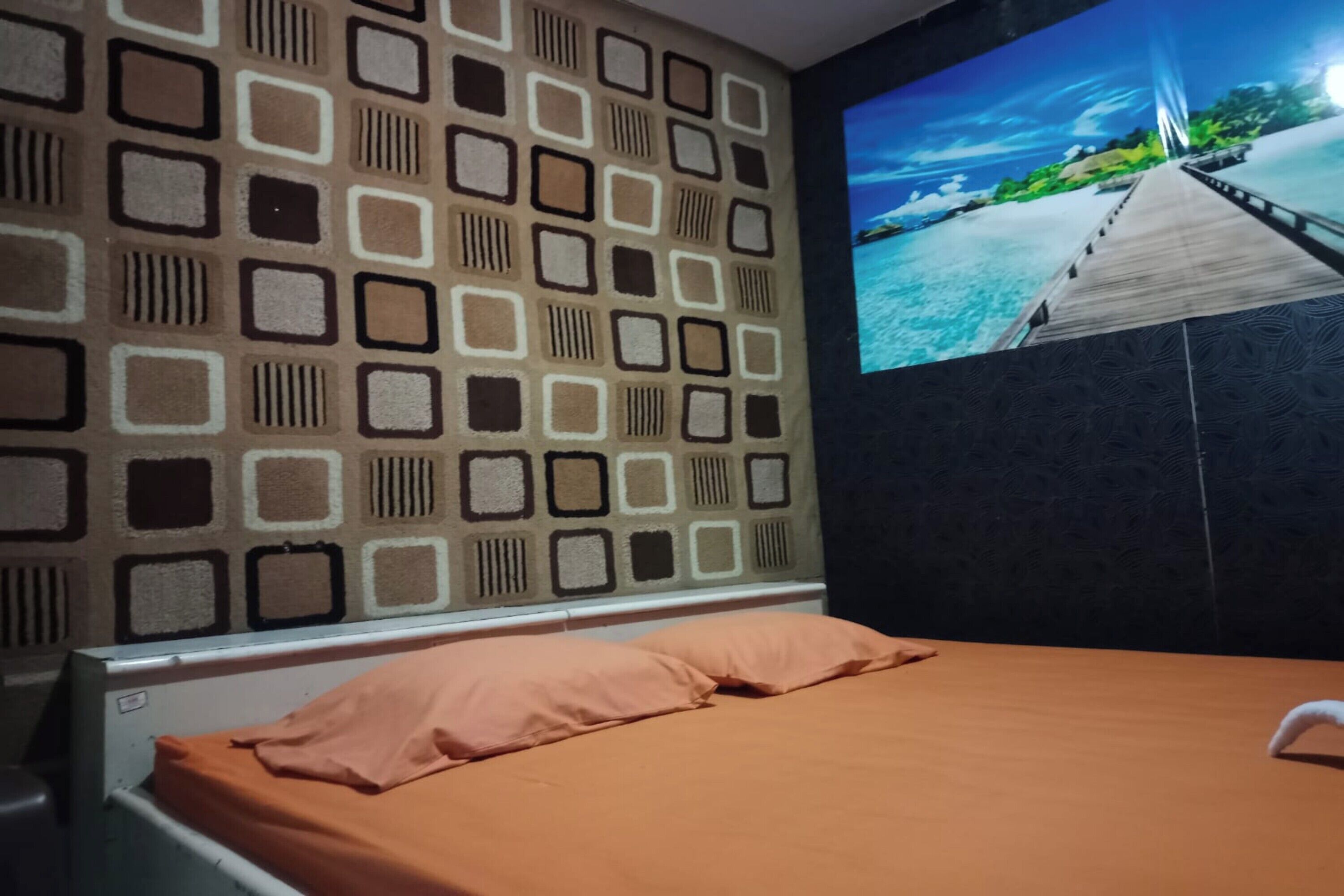 Quarto com cama, parede com padrão geométrico e uma tela grande exibindo uma paisagem.