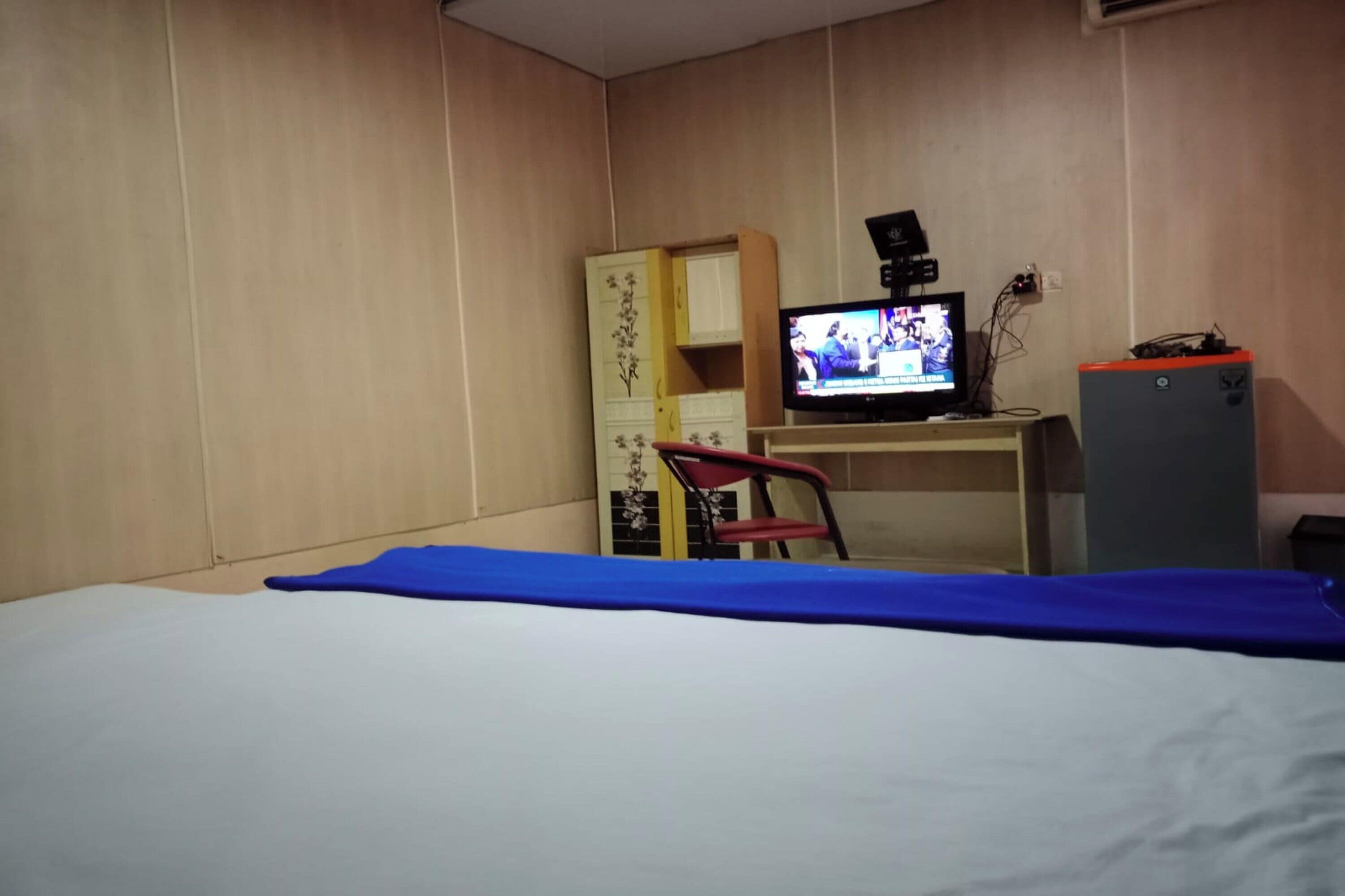 A room with a bed, a desk with a computer, a TV, and a chair.