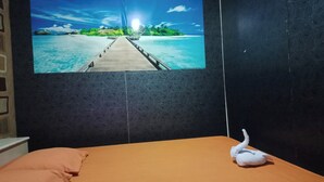 Un dormitorio con cama, almohada y televisión de pared mostrando una escena de playa.