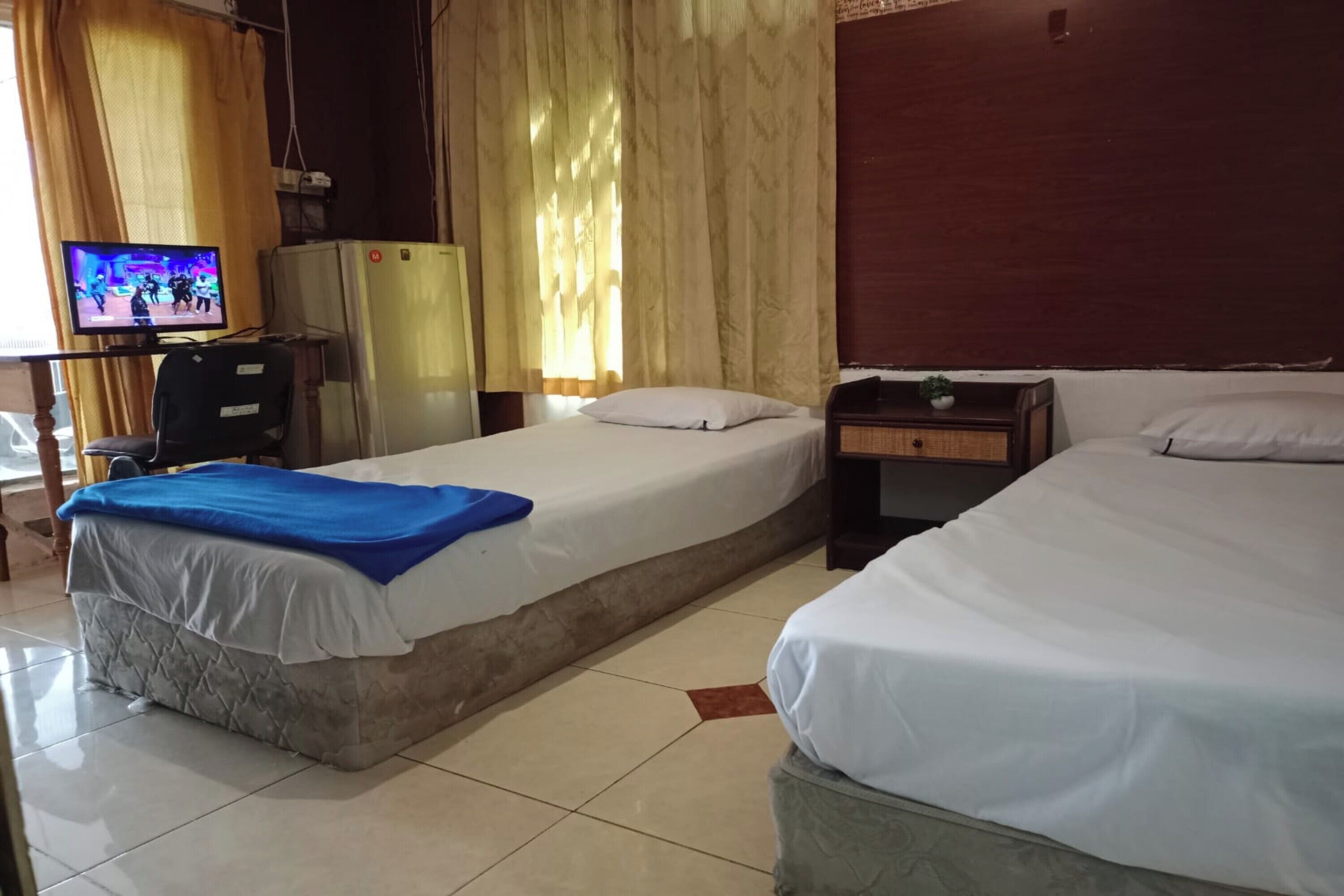 A hotel room with two beds, a television, a refrigerator, and a desk with a chair.