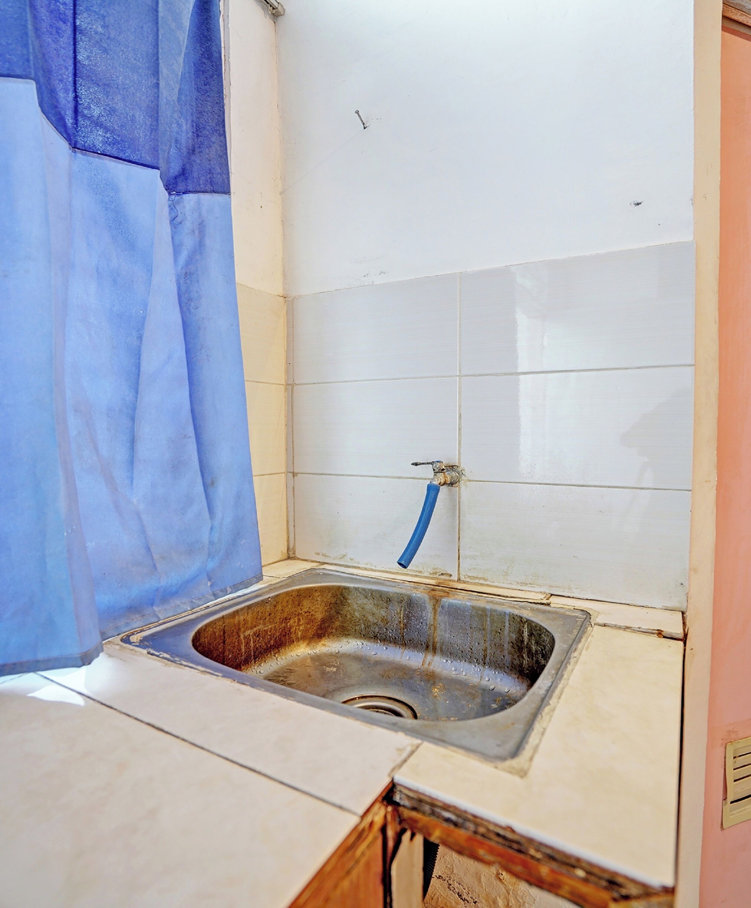 Cocina pequeña y funcional con un lavamanos, un grifo azul y un salpicadero de azulejos blancos.
