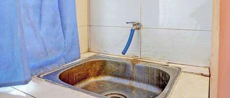 Cocina pequeña y funcional con un lavamanos, un grifo azul y un salpicadero de azulejos blancos.