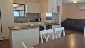 Une cuisine compacte avec des meubles blancs, une cuisinière et un coin repas comprenant une table en bois et des chaises blanches.