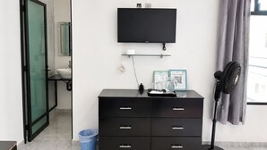 A modern room with a black TV on the wall, a black dresser with drawers, a blue laundry basket, and a standing fan. - La Palma Co-living (Tecamac)