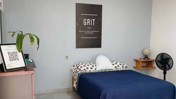 A bedroom with a bed, a desk, a wall-mounted fan, a globe, and a framed picture with a QR code.
