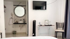 A hotel room with a large bed, a TV mounted on the wall, a small desk with a chair, and a bathroom visible through an open door. - La Palma Co-living (Tecamac)