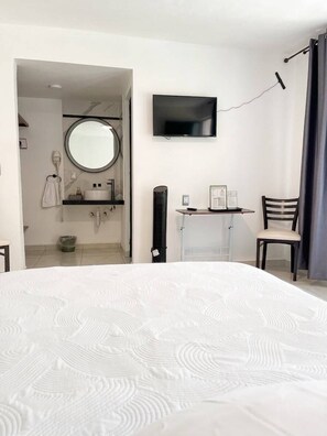 A hotel room with a large bed, a TV mounted on the wall, a small desk with a chair, and a bathroom visible through an open door. - La Palma Co-living (Tecamac)