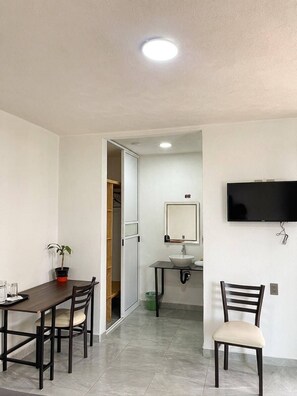 A room with a dining table, chairs, a TV mounted on the wall, a sink, and a mirror. - La Palma Co-living (Tecamac)