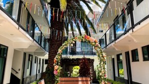 A modern building with a central atrium, a palm tree, and a floral archway. - La Palma Co-living (Tecamac)