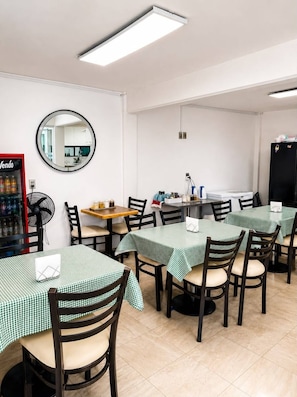 Un comedor con mesas redondas, sillas, una máquina expendedora y un refrigerador.