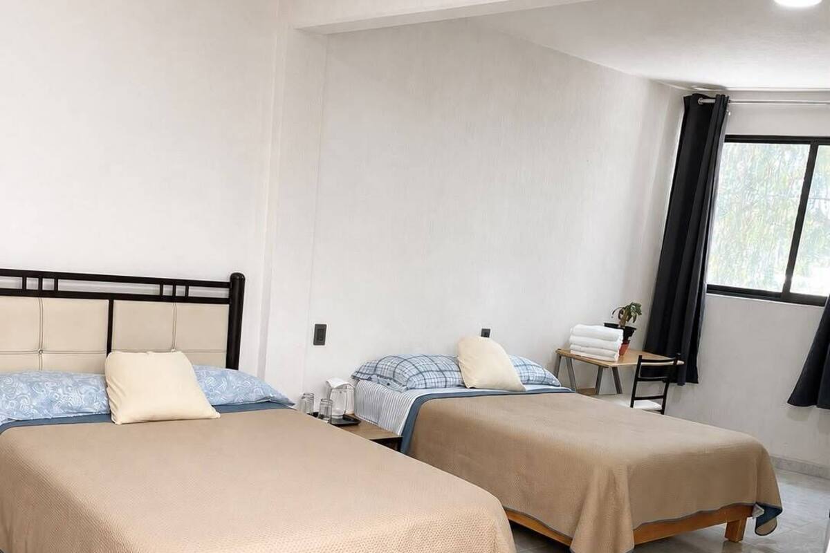 A hotel room with two beds, a small table, and a window with curtains.