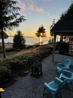 A patio with outdoor seating, a lantern, and a view of the sunset over water. - 01 - Coho Cottage Cottage By The Sea at Alder Bay (Port McNeill)