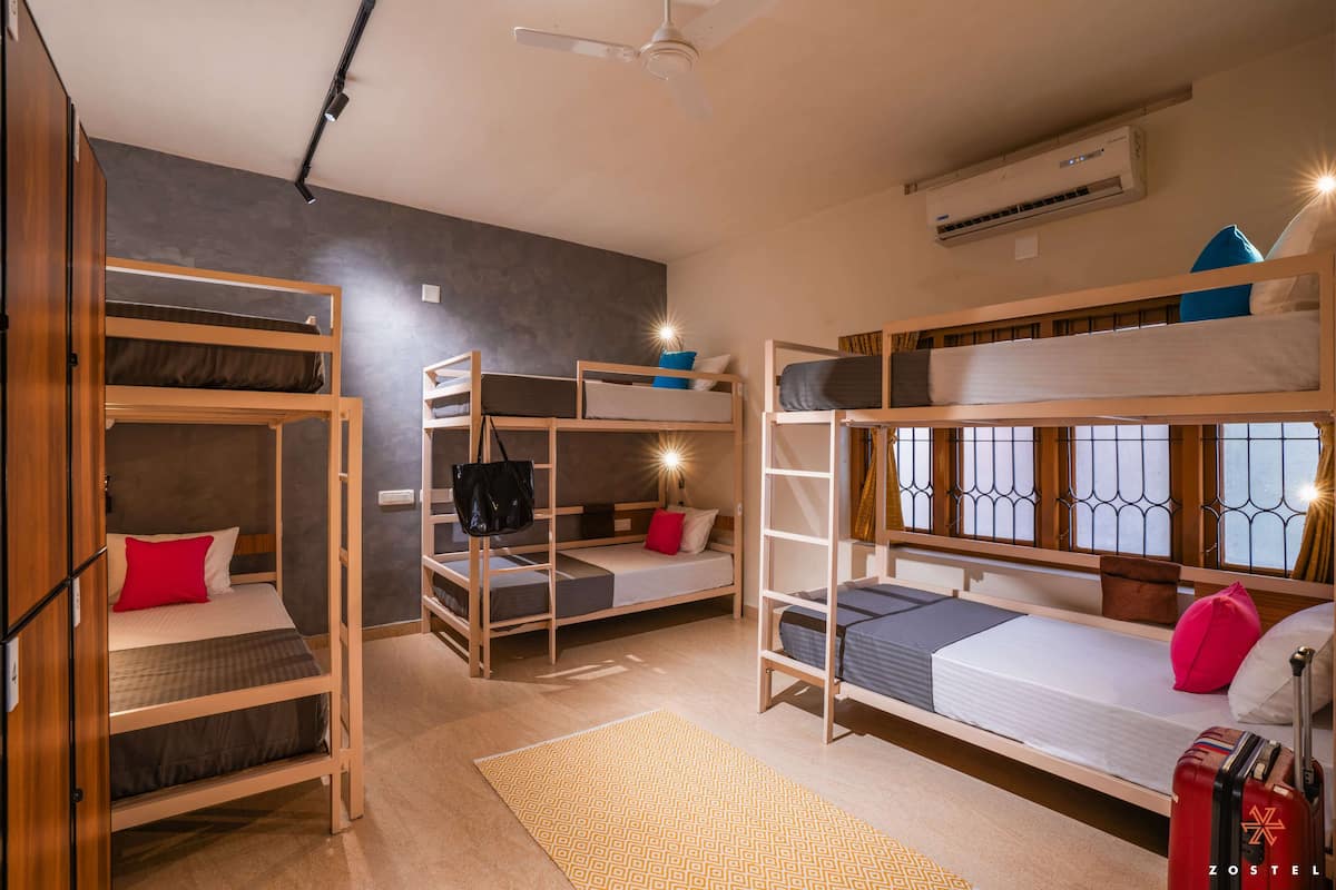 A dormitory room with bunk beds, a ceiling fan, an air conditioning unit, and a suitcase on the floor.