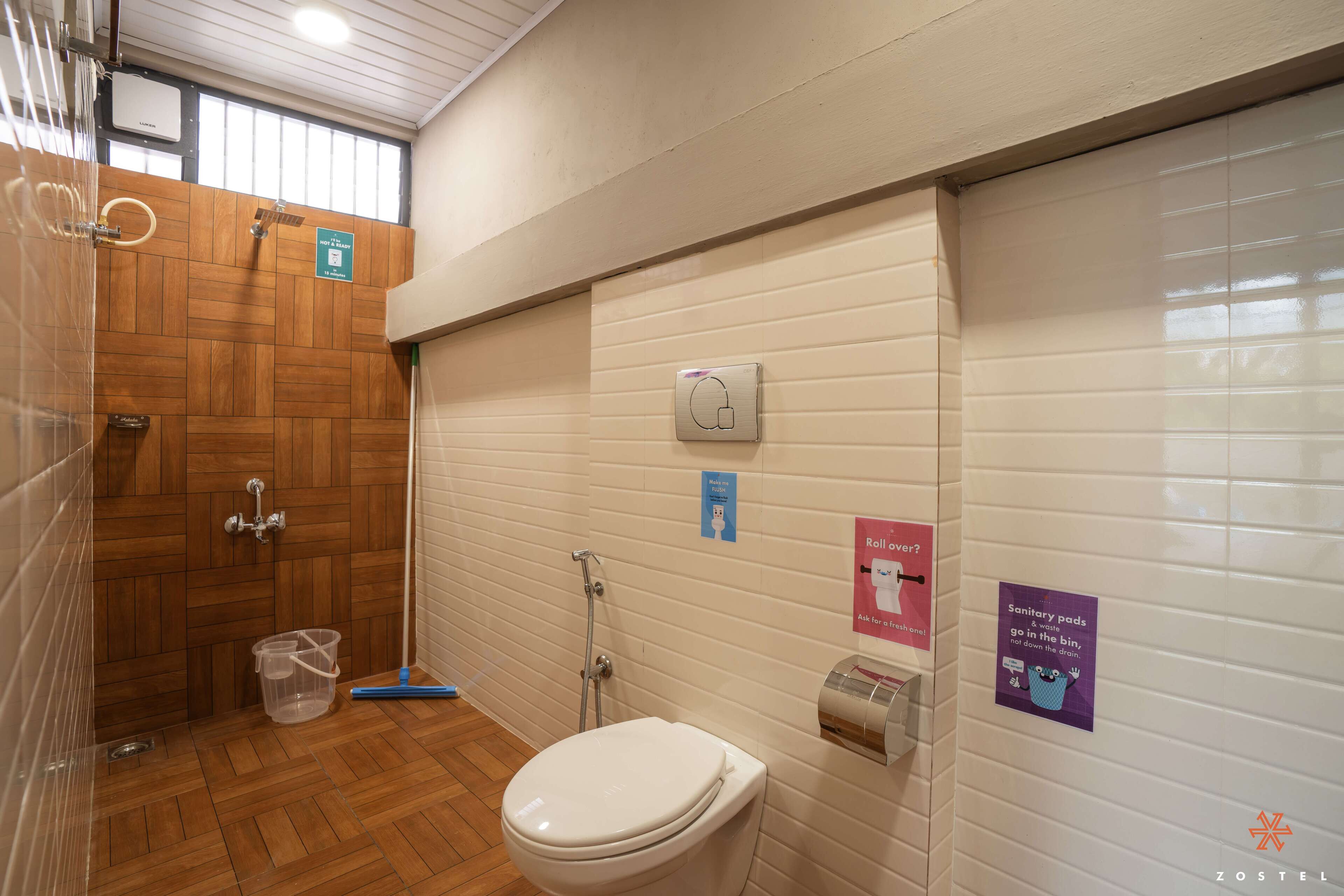A public restroom with a wooden shower enclosure, a toilet, and hand dryers.