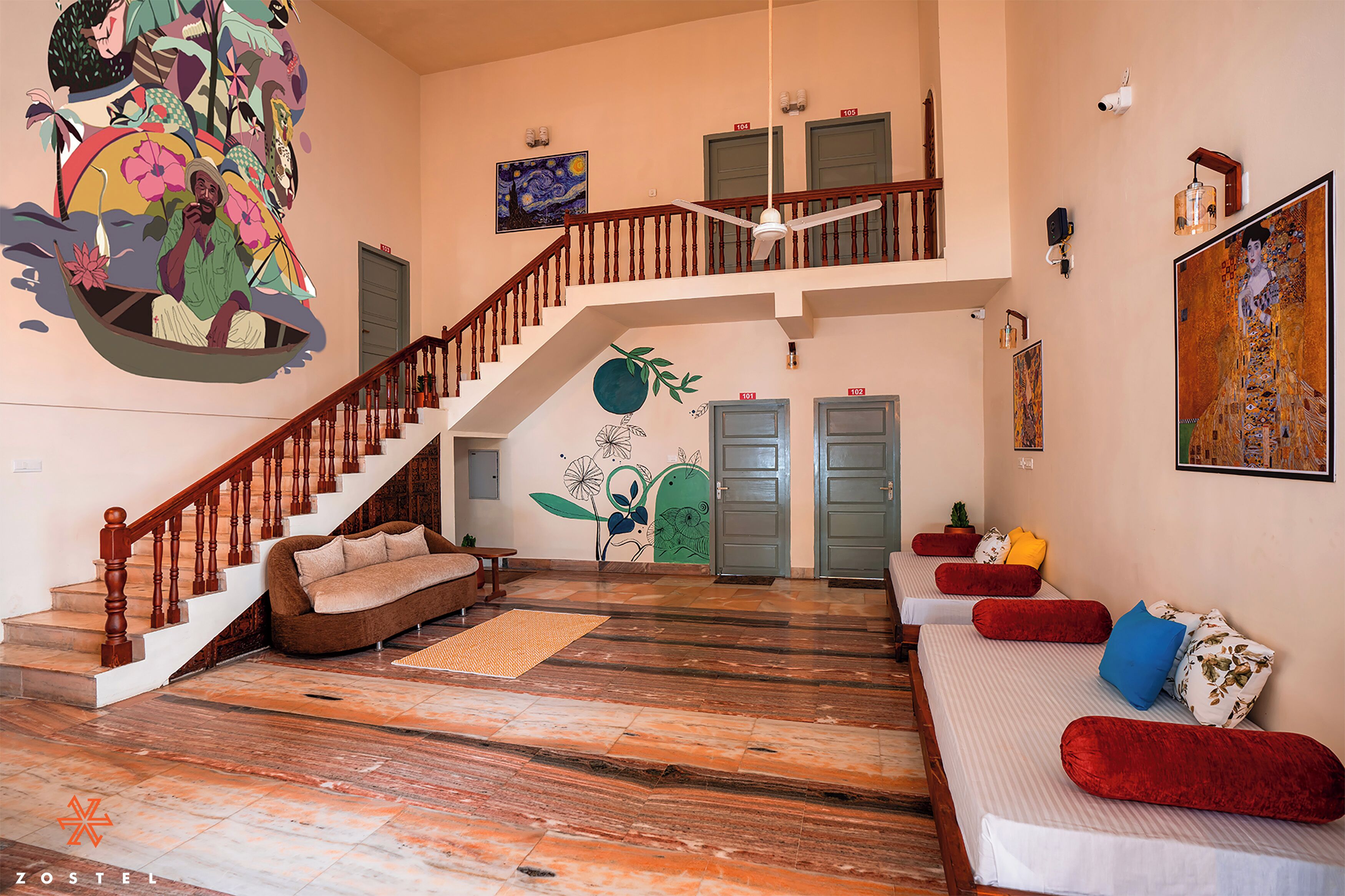 A spacious hotel lobby with a staircase, a sofa area, and a mural on the wall.