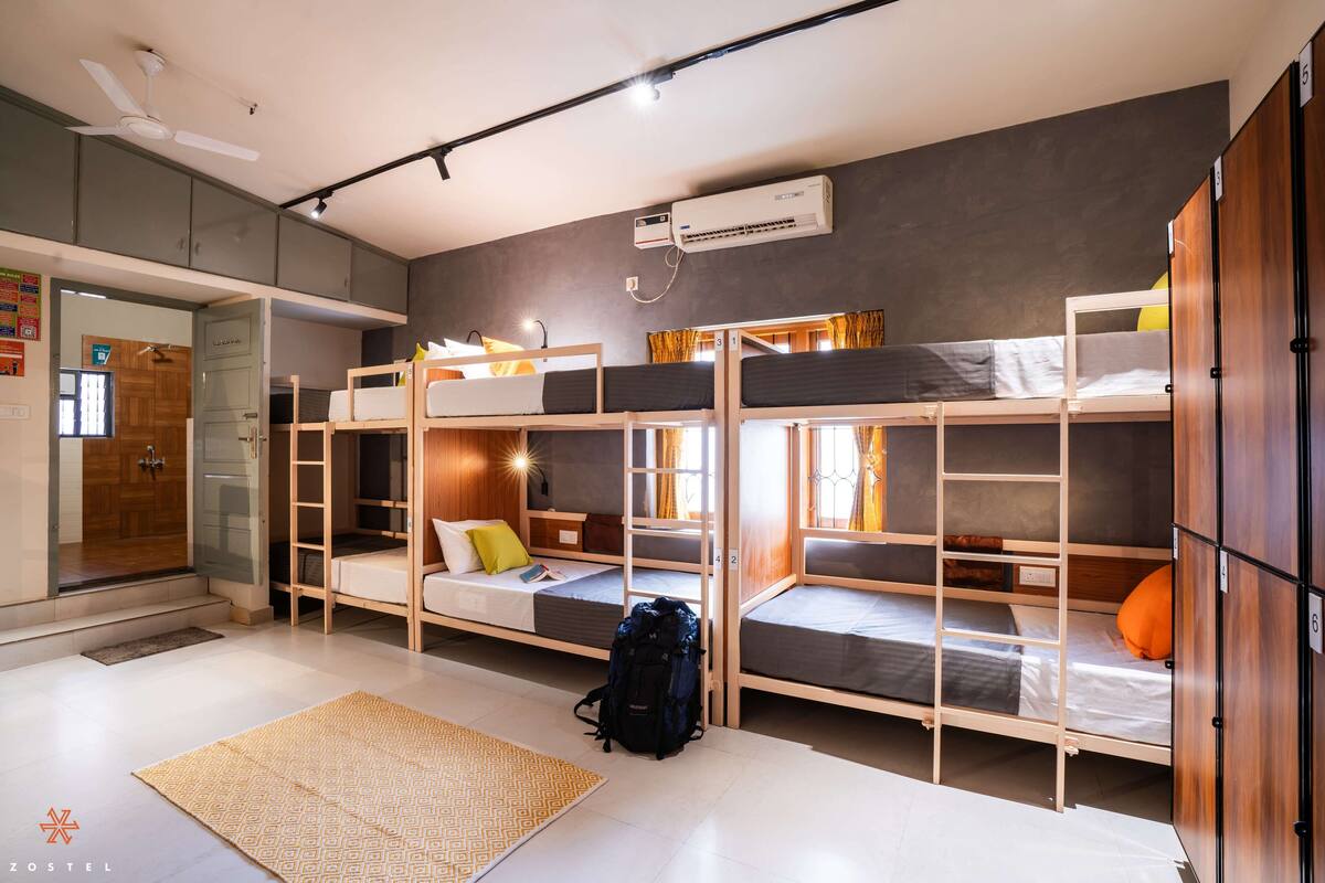 A dorm-style room with bunk beds, a ceiling fan, an air conditioning unit, and a visible door leading to another room.