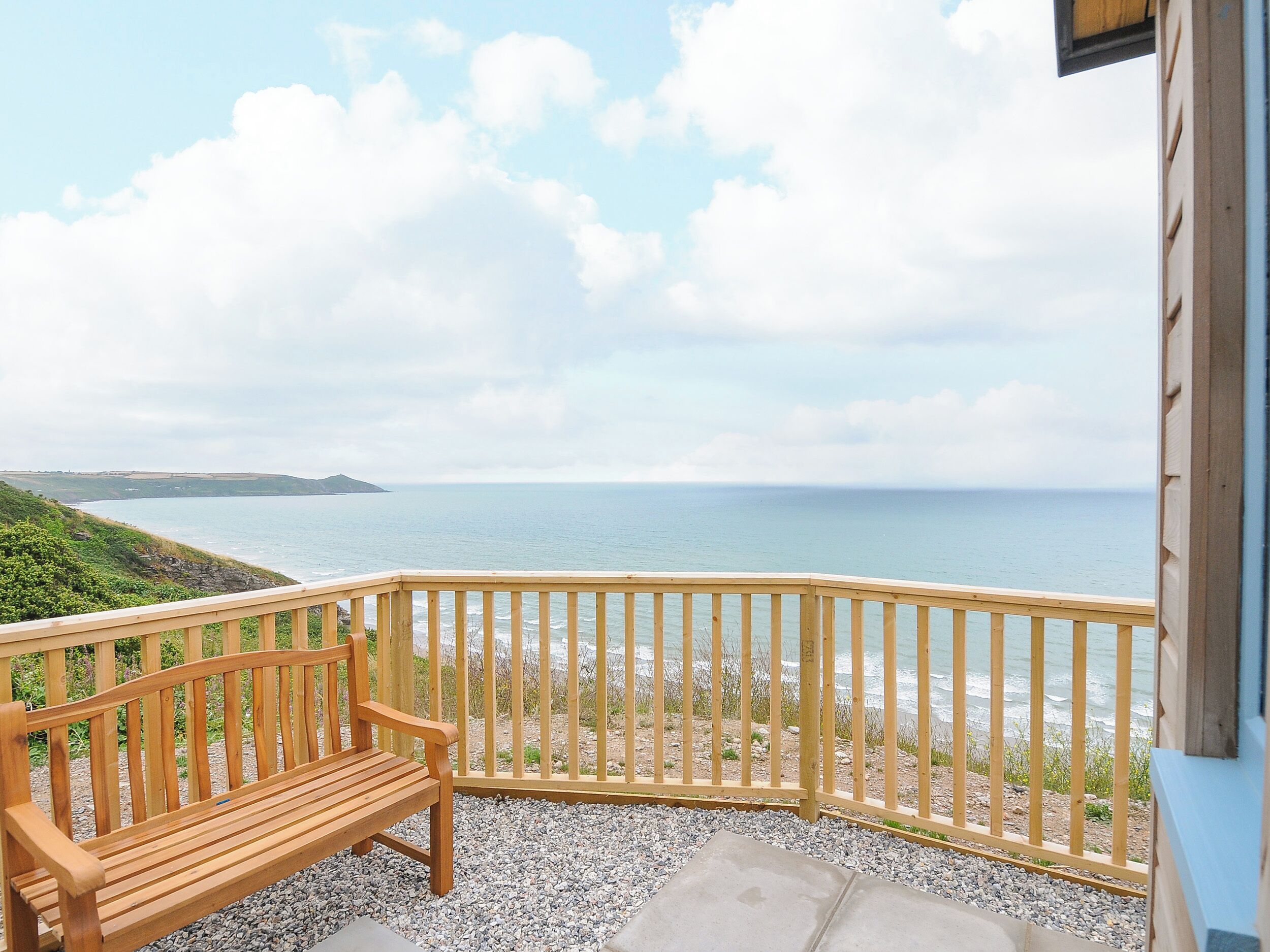 A wooden bench on a balcony with a view of the sea and a distant island.
