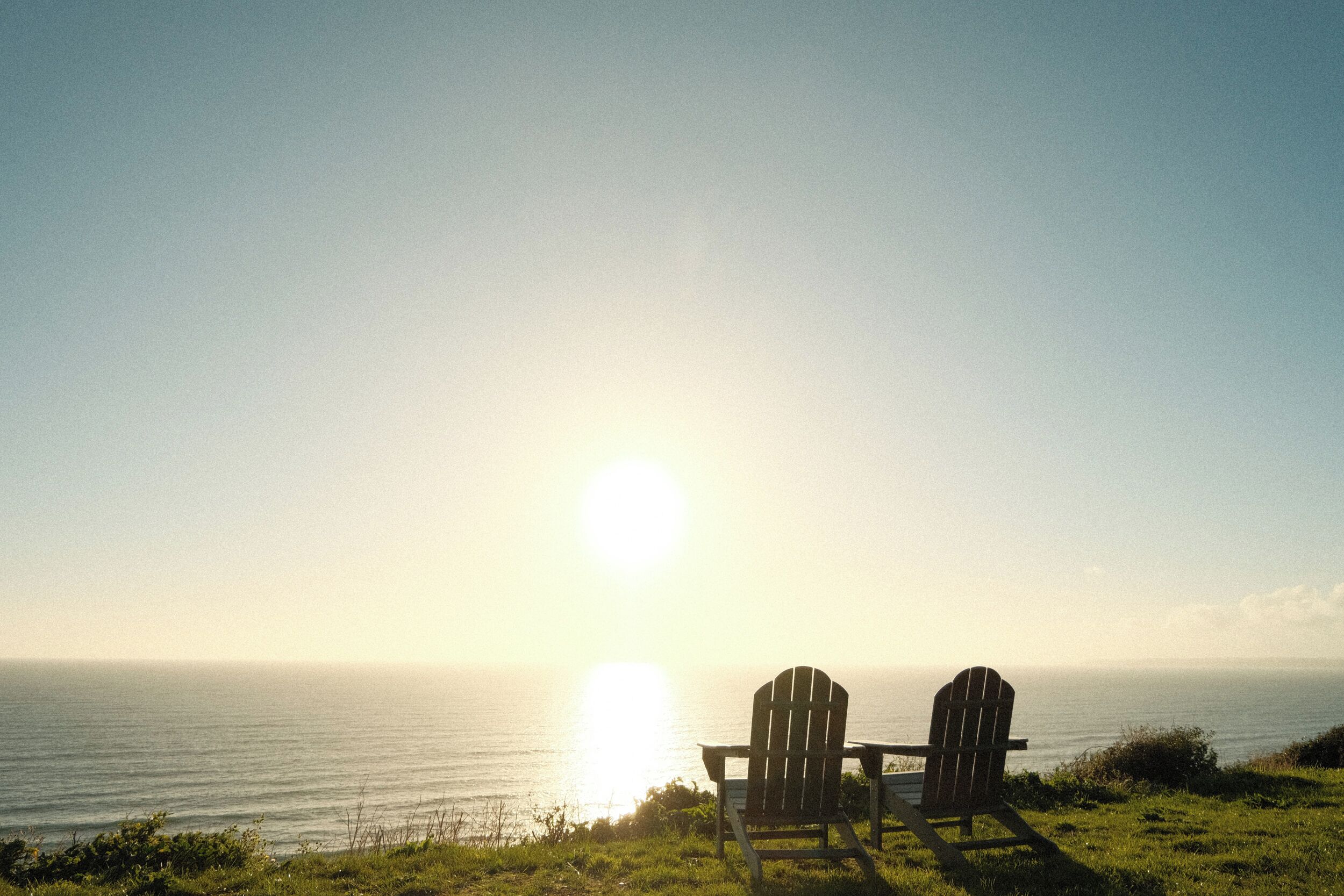 Two Adirondack chairs facing the ocean at sunset.