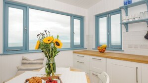 Una stanza con un tavolo in legno, un vaso con girasoli, una ciotola di frutta e vista sul mare attraverso finestre con cornice azzurra.