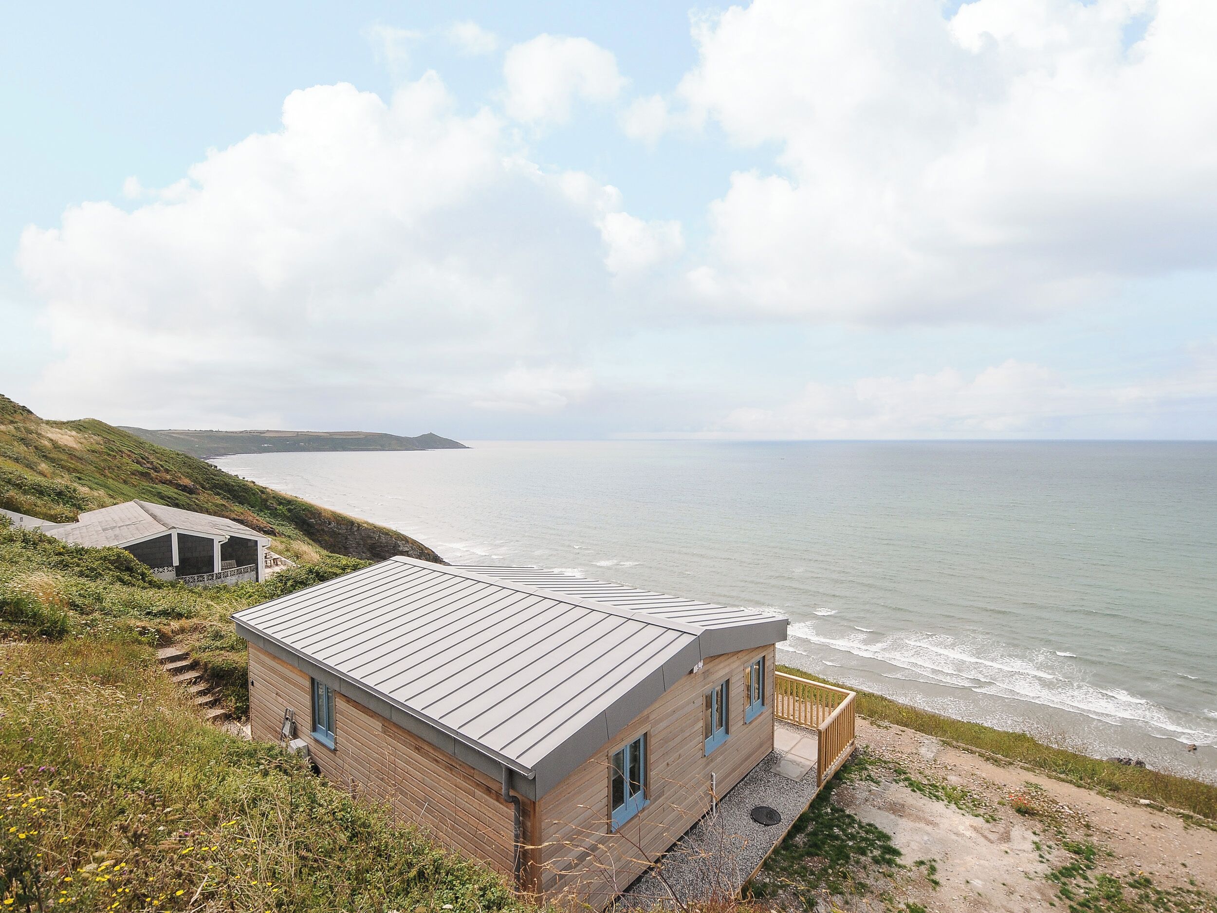 A coastal house with a metal roof, wooden walls, and a balcony overlooking the sea.