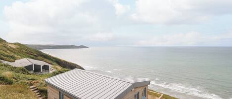 A coastal house with a metal roof, wooden walls, and a balcony overlooking the sea.
