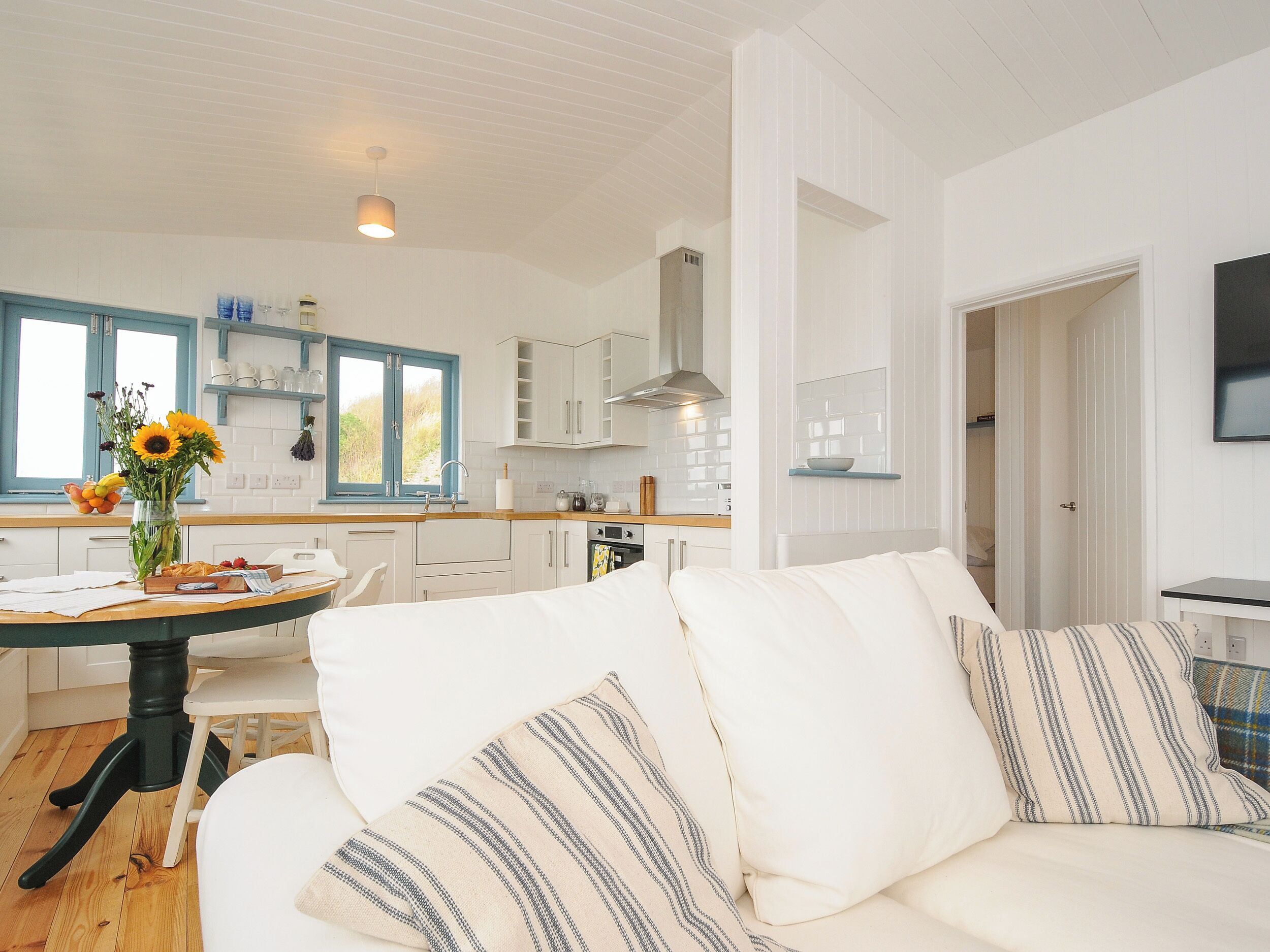 A modern kitchen with white cabinets, a dining table, and a sofa with striped cushions.