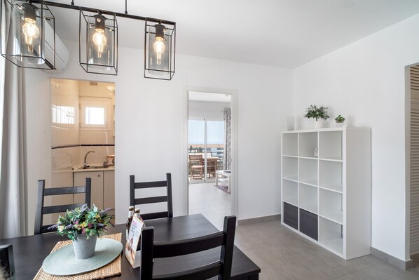 A modern kitchen with a window, a dining area with a table and chairs, and a white shelving unit.