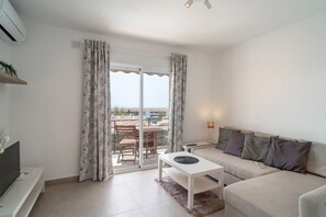 Ein modernes Wohnzimmer mit einer Couch, einem Couchtisch und einem Fernseher. Ein Balkon bietet Blick auf die Stadt.