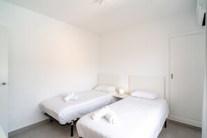 Hotelkamer met twee eenpersoonsbedden, elk met witte lakens en kussens, een nachtkastje met lamp en een kledingkast.