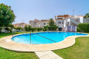 A swimming pool with a metal ladder, surrounded by a grassy area and a building with a tiled roof.
