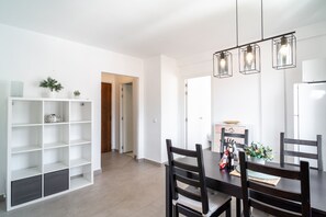 Een moderne eethoek met een houten tafel, zwarte stoelen en hanglampen. Er is een wit wandrek met planten en decoratieve objecten.