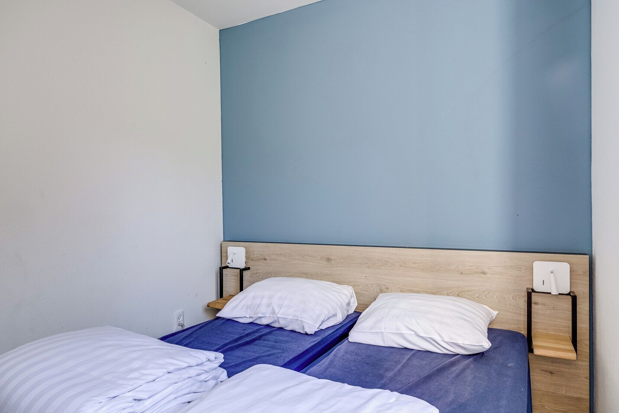 Ein Zimmer mit zwei Betten, einem hölzernen Kopfteil und einer Wandleuchte.