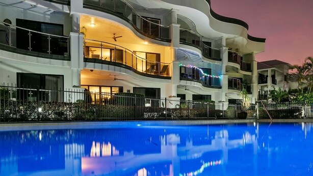 Um hotel com vários andares, varandas, piscina e céu ao pôr do sol.
