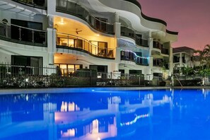 Un hotel a più piani con balconi, una piscina e un cielo al tramonto.
