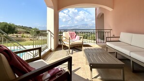 A balcony with a view of the countryside, a white sofa, a table, and a chair with a blanket. - Villa Eleftheria: 4 bedrooms for up to 9 adults, pool and outstanding 180° views (Lakithra)