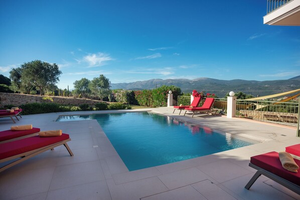 A swimming pool with red lounge chairs and a view of mountains.