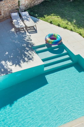 Una piscina con un cerchio gonfiabile colorato, sedie a sdraio e un muro in pietra sullo sfondo.