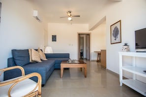 Un soggiorno con un divano blu, un tavolino in legno, una ventola a soffitto e un mobile TV bianco.