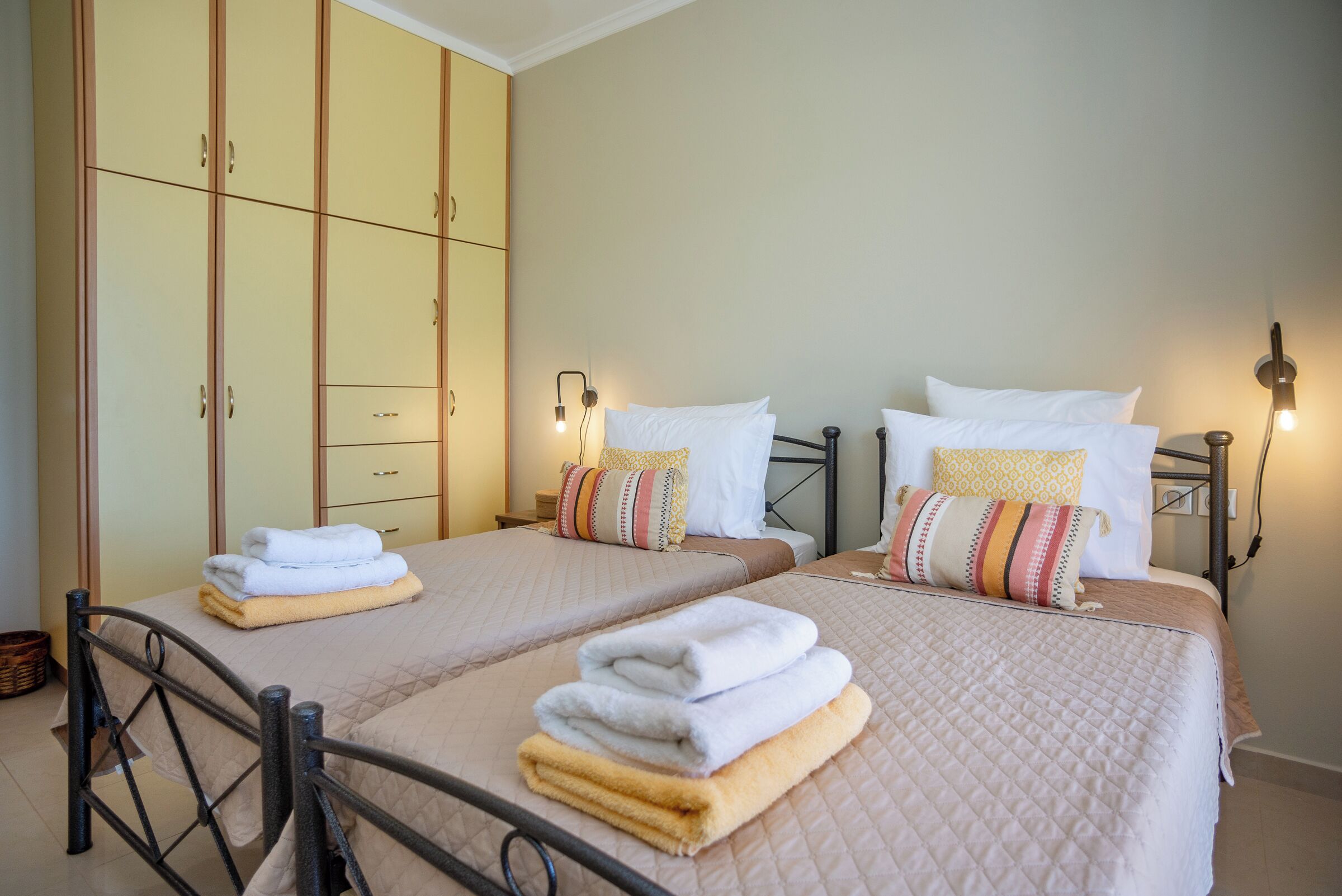 A hotel room with two beds, each with a quilted bedspread and pillows, a wardrobe with multiple doors, and bedside lamps.