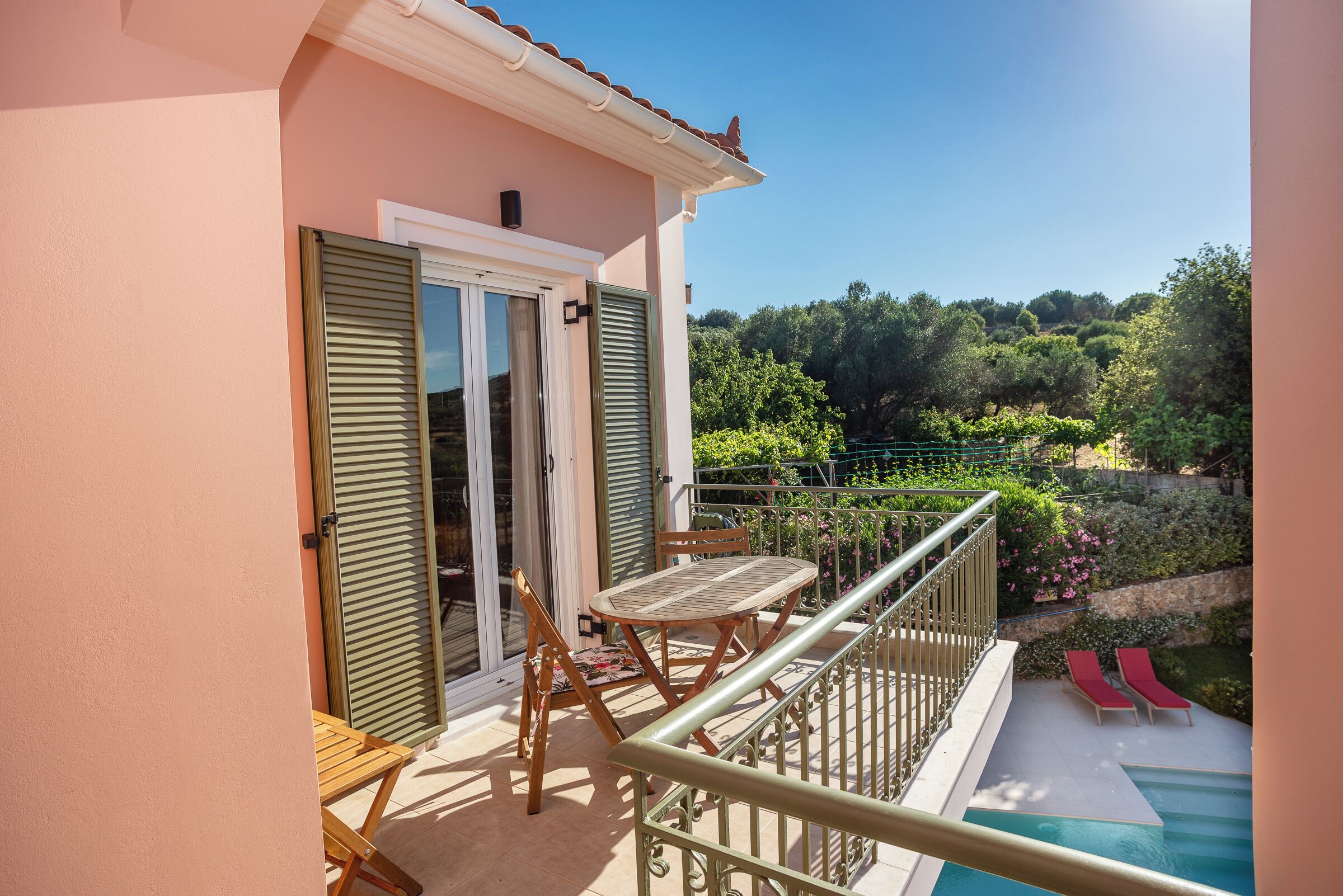 A balcony with a table and chairs, a pool, and a view of a garden.