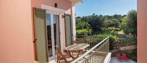 A balcony with a table and chairs, a pool, and a view of a garden.