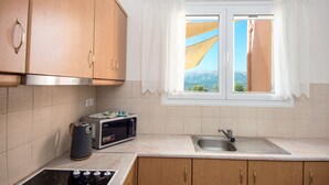 A kitchen with wooden cabinets, a microwave, a kettle, and a window with a view of the outdoors. - Villa Eleftheria: 4 bedrooms for up to 9 adults, pool and outstanding 180° views (Lakithra)