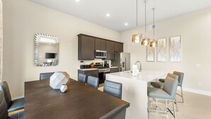 A modern kitchen with dark cabinets, a microwave, and a refrigerator. There is a dining area with a large table and chairs.