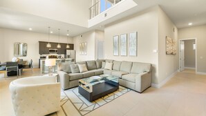 A spacious living room with a sectional sofa, a glass coffee table, and a high ceiling with skylights.