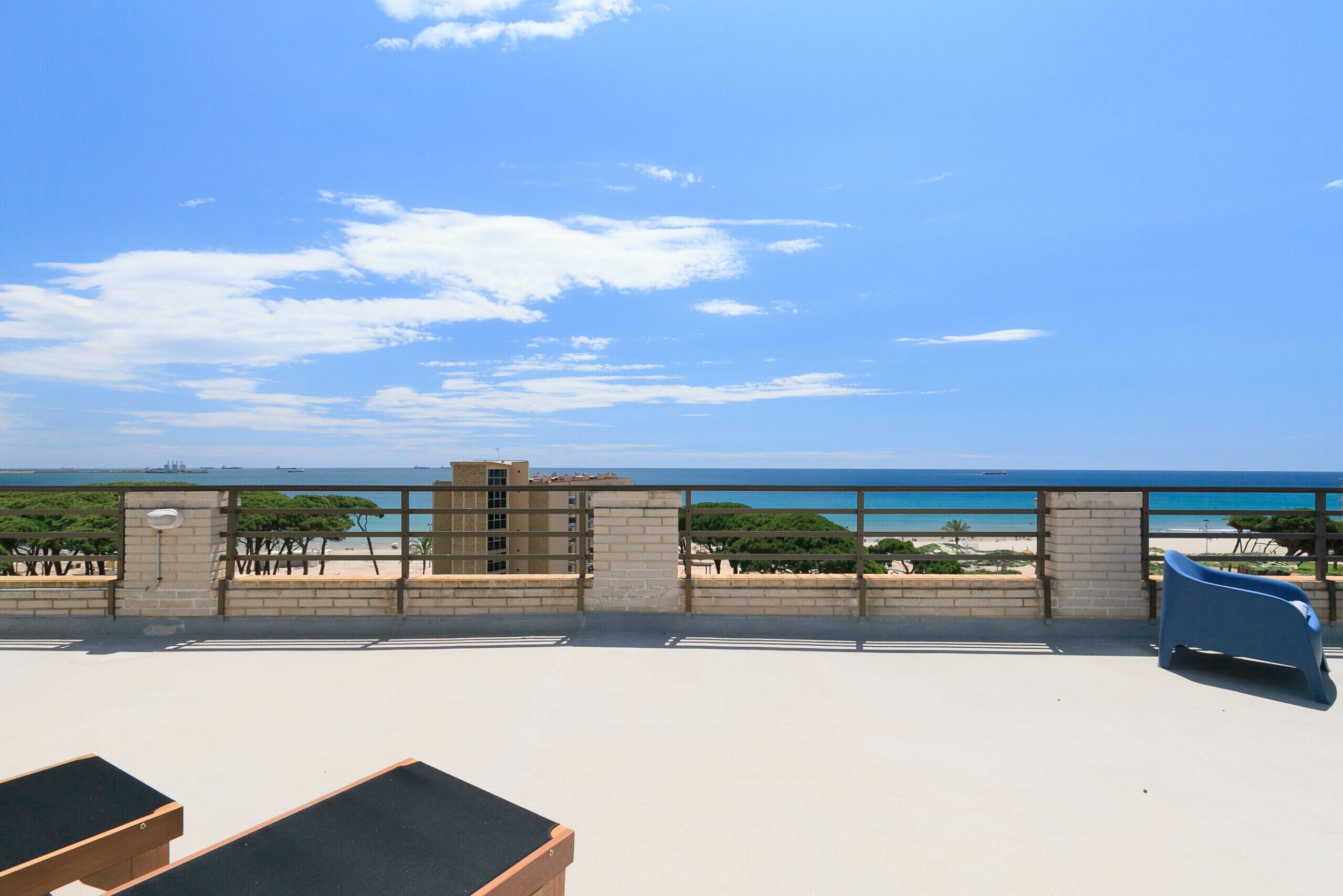 A rooftop terrace with a view of the beach, a blue chair, and a wooden bench.
