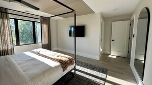 Een moderne slaapkamer met een hemelbed, een tv aan de muur en een grote spiegel.